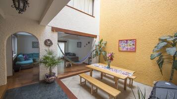Un espacio interior acogedor con una mesa de madera y bancos, una hamaca y una planta en maceta.