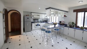 Una cocina con armarios blancos, una isla central con taburetes de bar, un refrigerador y una estufa.