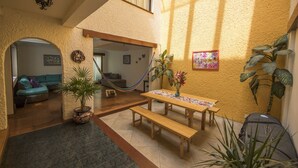 Un espacio interior acogedor con un banco de madera, una hamaca y una mesa de comedor con mantel colorido.
