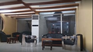 Ein modernes Wohnzimmer mit einer Couch, Sesseln und einem Couchtisch. Ein großes Fenster bietet einen Blick ins Freie.