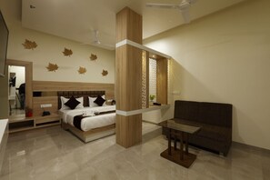A modern hotel room with a large bed, a sofa, a glass table, and decorative leaf wall art. - Hotel Alka Inn (Ahmedabad)