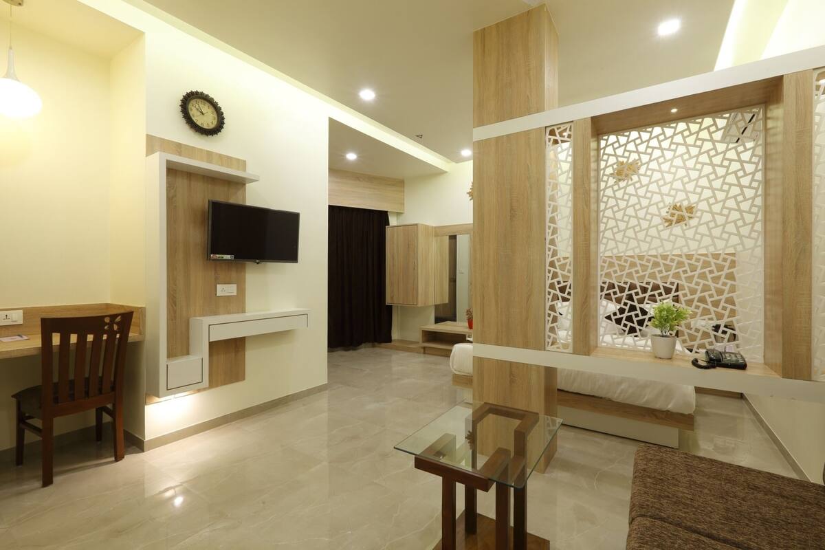 A modern living room with a glass coffee table, wooden furniture, a flat-screen TV, and a decorative partition.