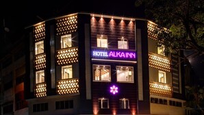 Un bâtiment sur lequel on peut lire l’inscription « HÔTEL ALKA INN » et qui arbore un symbole représentant une fleur violette.