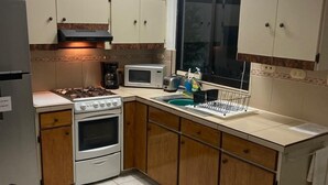 A compact kitchen with a gas stove, microwave, and oven. There is a window with a view of greenery outside. - Brisas del Caribe Suite (Playa del Carmen)