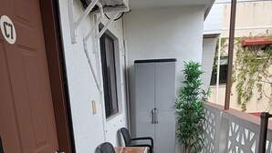 A small outdoor area with a brown door, a white wall, a grey cabinet, two black chairs, a small table, a potted plant, and a decorative white fence. - Brisas del Caribe Suite (Playa del Carmen)