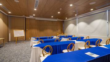 A conference room with tables covered in blue tablecloths, white chairs with gold headrests, and a whiteboard on a stand.