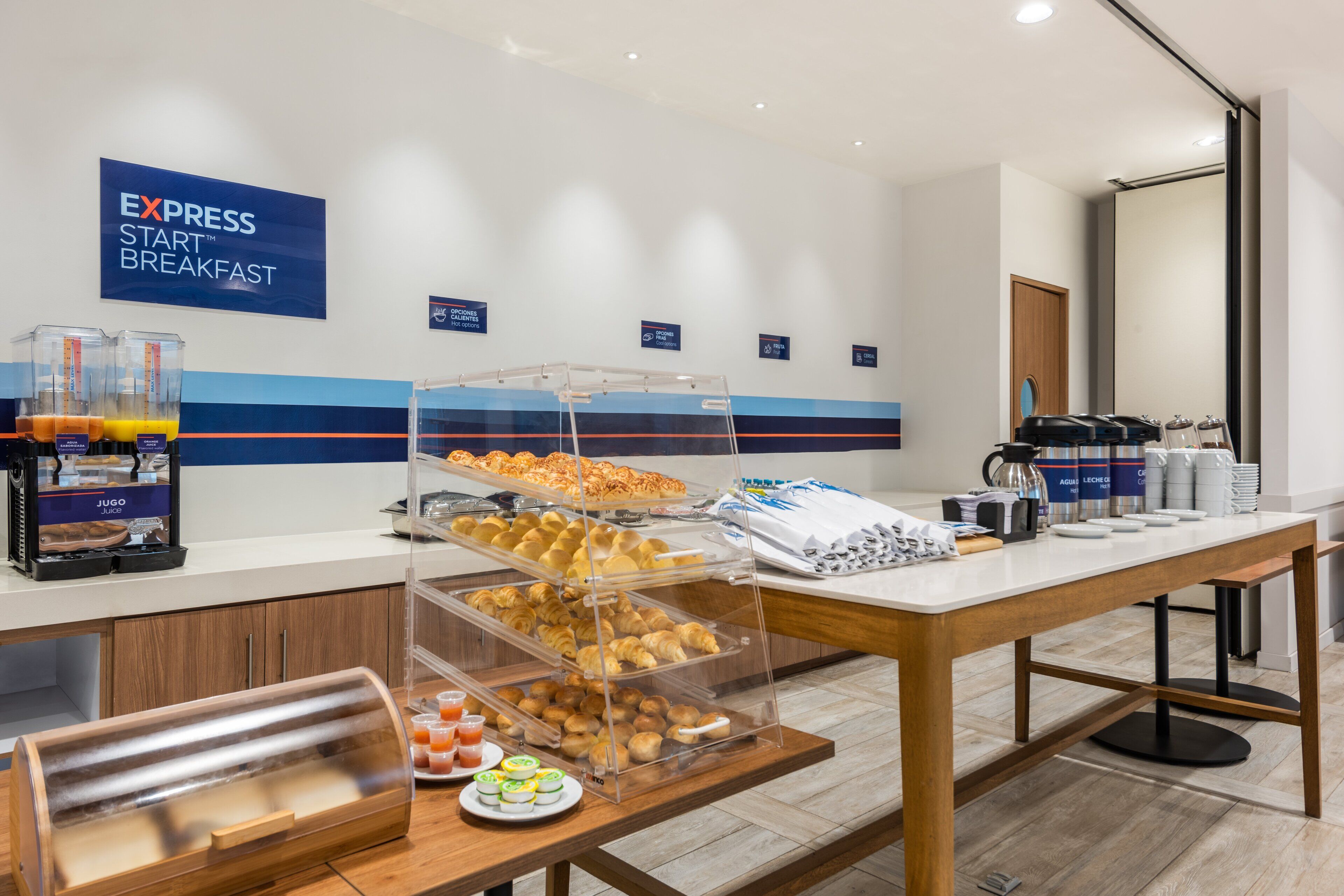 Un buffet de petit-déjeuner proposant diverses pâtisseries, un distributeur de jus de fruits et des machines à café.