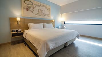 Quarto de hotel moderno com uma cama grande, um mapa na parede e vista da cidade.