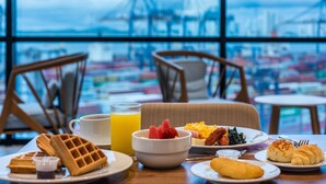 A breakfast table with waffles, fruit, eggs, and croissants, with a view of a port and cranes in the background. - Holiday Inn Express Cartagena Manga by IHG (Cartagena)