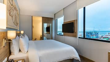 Una habitación de hotel moderna con una cama grande, un televisor de pantalla plana en la pared y un ventanal con vistas al puerto.