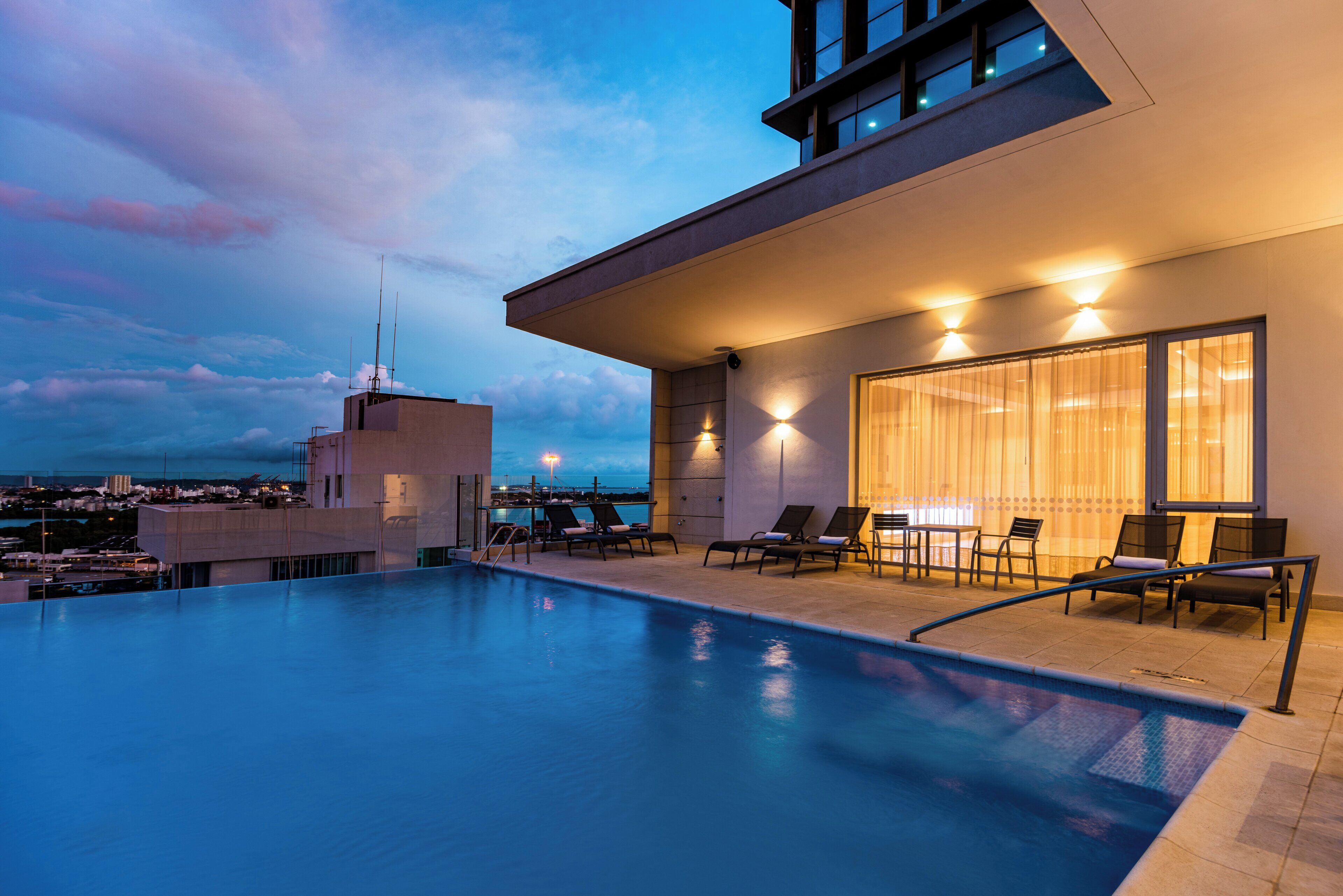 Zona de piscina en la azotea con sillones y vistas al horizonte de la ciudad.