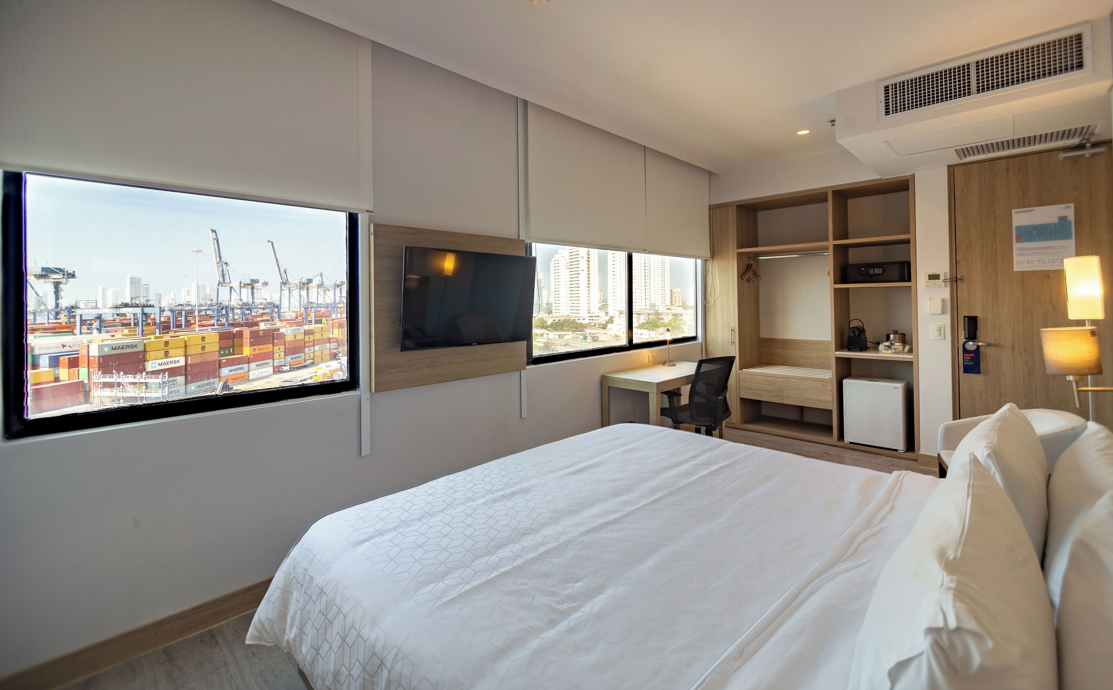 A hotel room with a large bed, a desk with a chair, a TV, and a wardrobe.