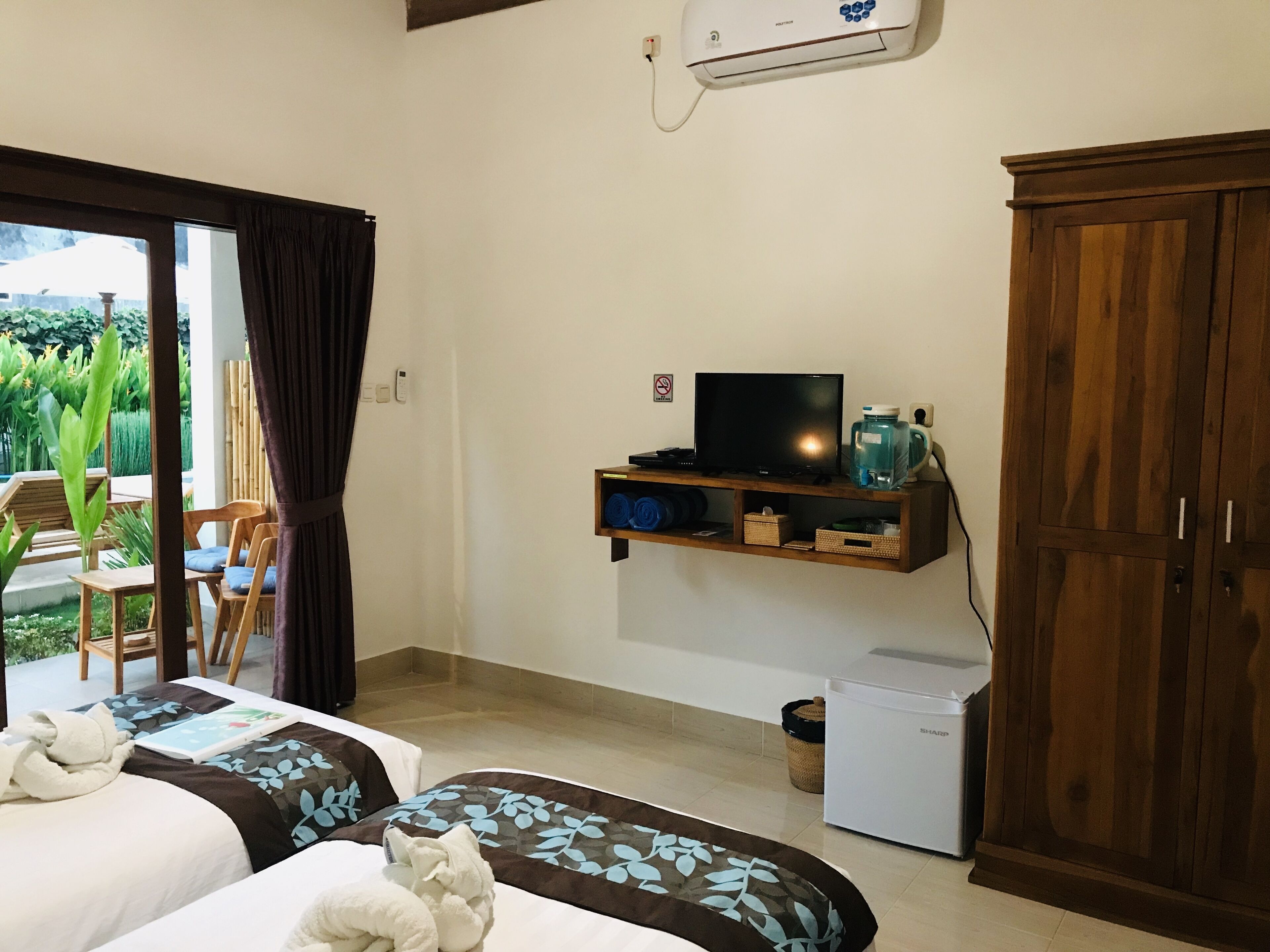 A hotel room with two beds, a TV, a small fridge, and a wooden wardrobe.