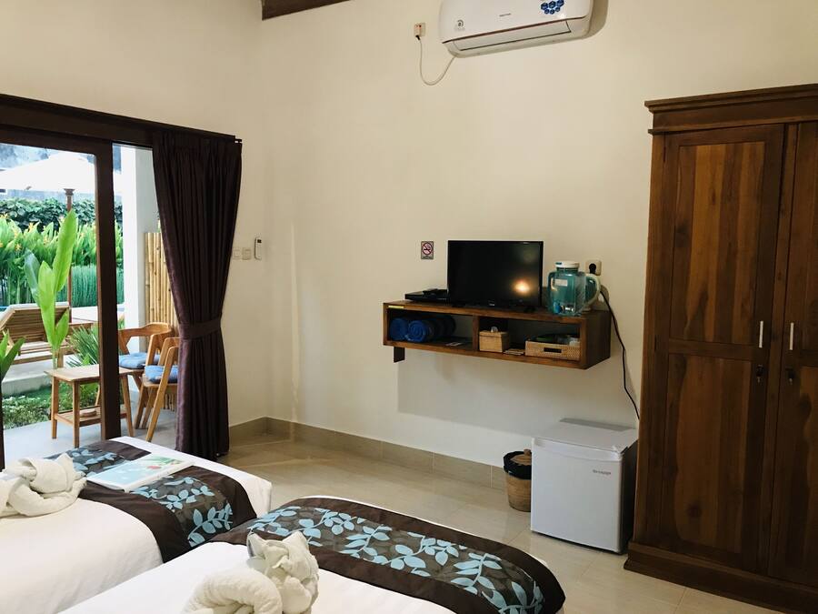 A hotel room with two beds, a TV, a small fridge, and a wooden wardrobe.