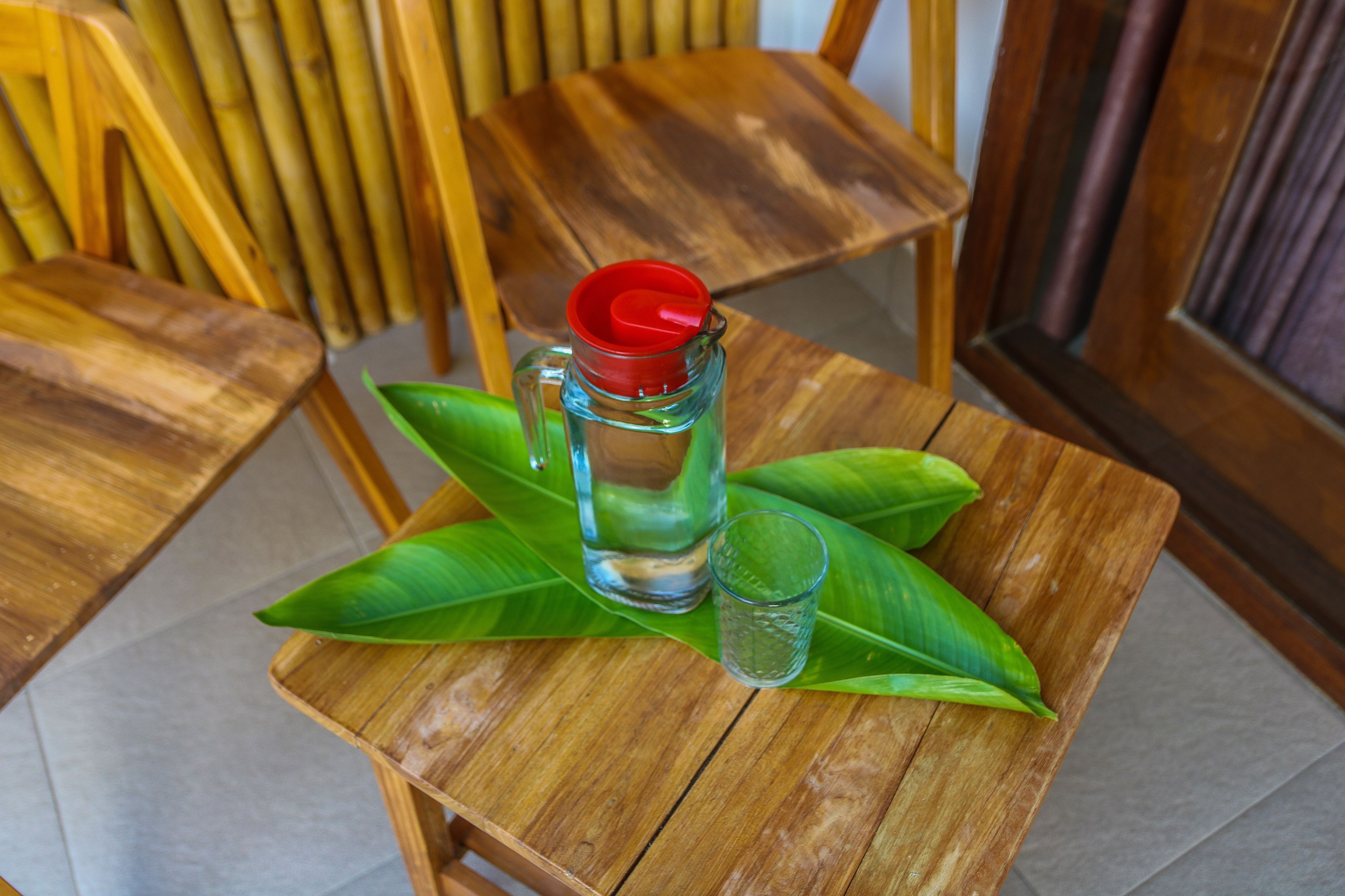 Ett träbord med en genomskinlig glasbringa och ett glas placerat på ett grönt blad.