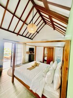 Un dormitorio amplio con una cama grande, vigas de madera, un ventilador de techo y vistas al exterior.