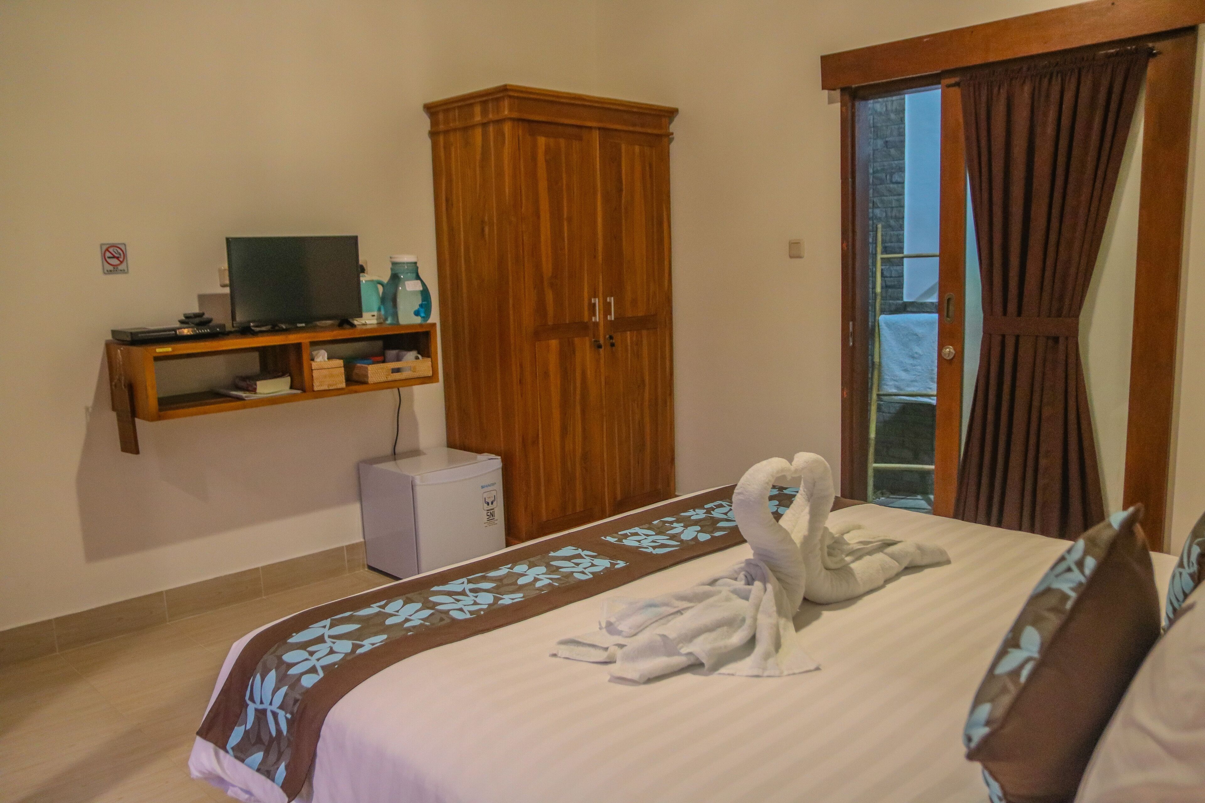 Une chambre d’hôtel avec un lit, une armoire en bois, un téléviseur posé sur une étagère et une vue à travers une porte vitrée.