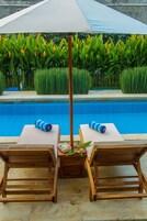 Zona junto a la piscina con dos sillones de madera, una mesa y un gran paraguas.