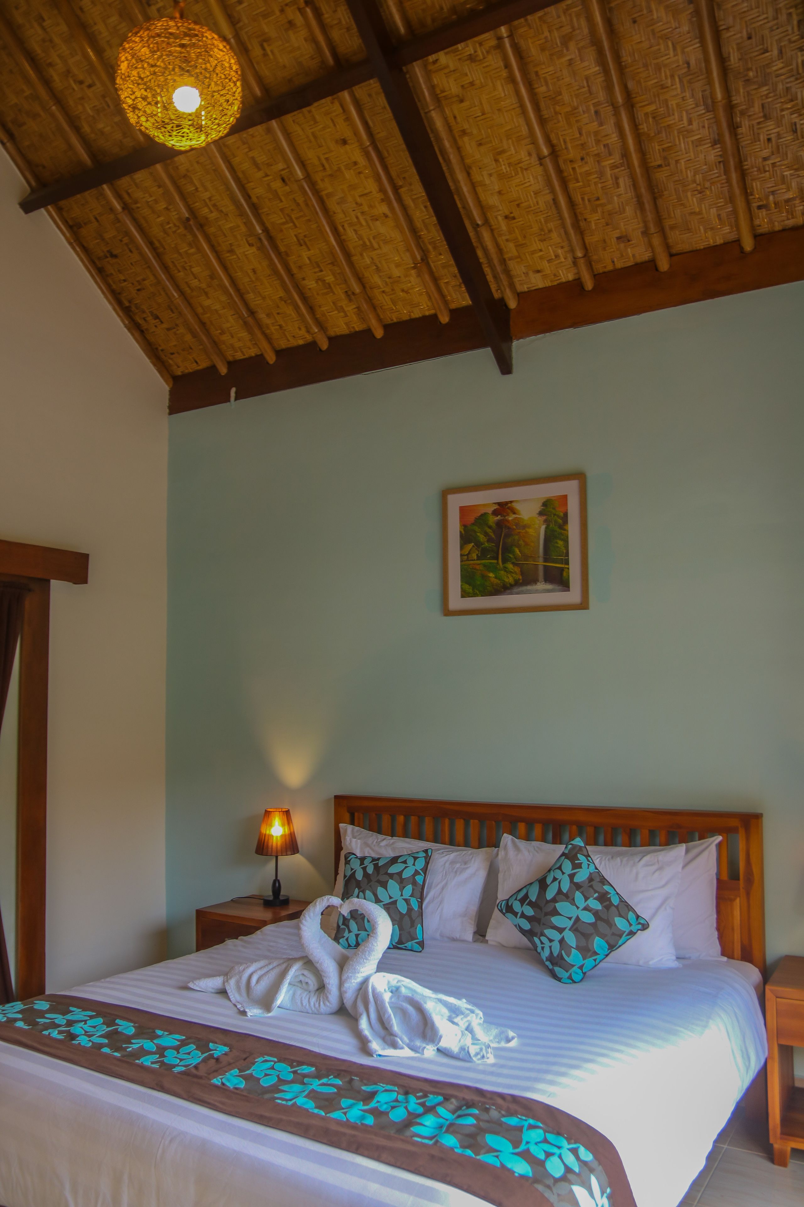 A hotel room with a bed, a nightstand, a lamp, a framed picture on the wall, and a ceiling with a woven design.