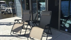 A covered outdoor seating area with two lounge chairs and a view of a marina with boats. - FLOATING Apartment. Enchanting Lake Views, Sunsets, FUN (Monroe)