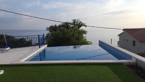 A swimming pool with a view of the sea, a blue railing, and a grassy area.