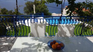 A balcony with a view of a swimming pool, a table with a fruit bowl, and a blue railing.