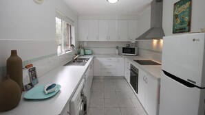 A compact kitchen with white cabinets, a microwave, a toaster, and a refrigerator. - CHILL-OUT BEACHSIDE * coastal cool on Main Beach. Stroll to cafes, shops & lake! (Forster)