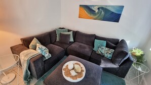 A modern living room with a sectional sofa, a small round table with decorative shells, and a minimalist side table. - CHILL-OUT BEACHSIDE * coastal cool on Main Beach. Stroll to cafes, shops & lake! (Forster)