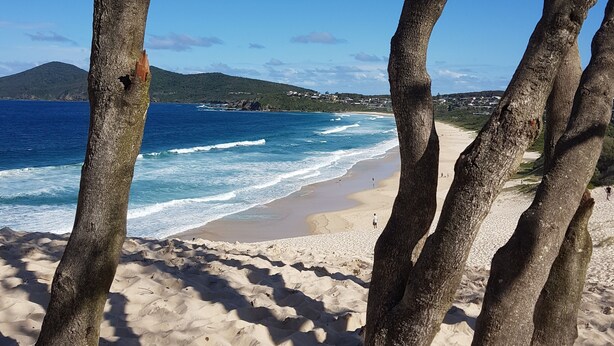 Une plage de sable fin, avec une eau d’un bleu limpide et une vue sur une chaîne de montagnes lointaine.