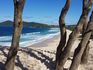 A sandy beach with clear blue water and a view of a distant mountain range.