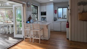 Une cuisine moderne avec des meubles blancs, un four à micro-ondes encastré et une machine à café. On y trouve un coin repas avec des chaises et une table blanches, ainsi qu’une grande fenêtre qui laisse entrer la lumière naturelle.