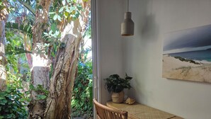 Une table en bois, une chaise en osier, une suspension, une plante en pot et un tableau représentant une plage, le tout disposé dans la pièce.