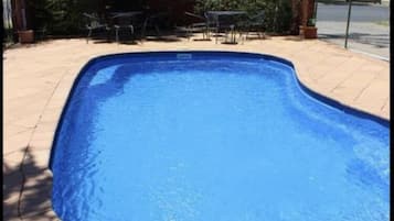Une piscine dotée d’une terrasse carrelée, entourée d’arbres et d’une clôture.