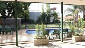 A covered outdoor area with a pool, green chairs, and potted plants.