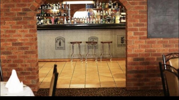 A bar area with a brick archway, a counter with various bottles, and three stools.