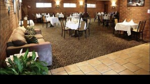 A restaurant with brick walls, multiple tables and chairs, and a patterned carpet.
