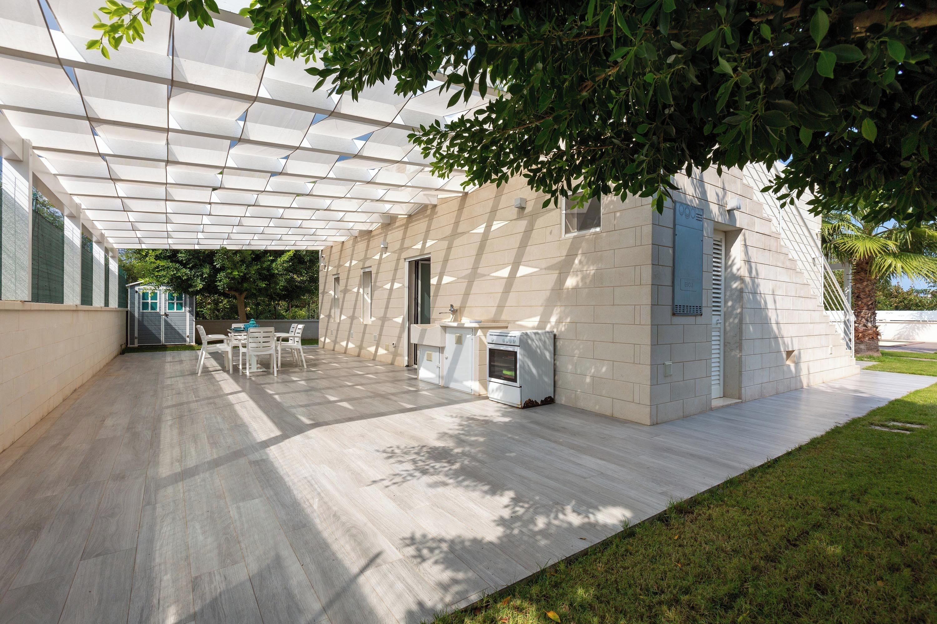 Un patio couvert au design moderne, doté d’un toit plat, d’un espace salon avec des chaises et d’un four encastré.