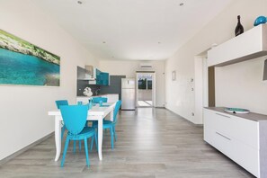 A modern kitchen with white cabinets, a dining area with blue chairs, and a large painting of a coastal scene.