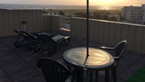 En takterrass med ett bord och stolar, ett parasoll och utsikt över havet och stadsbilden.
