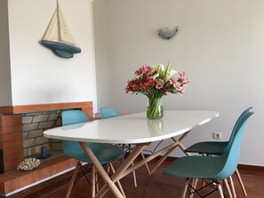 A dining area with a white table, teal chairs, and a vase of flowers. - Cozy Beach Front with Rooftop (Vila do Conde)