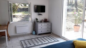 A room with a TV mounted on the wall, a white dresser, a radiator, a window, and a potted plant. - In the heart of nature, a welcoming nest with swimming pool to recharge your batteries (Barjols)