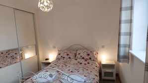 A bedroom with a bed, two bedside tables, a mirror, and a hanging light fixture.