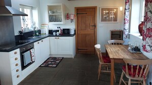 A kitchen with white cabinets, a wooden door, a dining table with chairs, and a tiled floor.