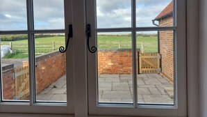 A view through a window with a metal handle, revealing a brick wall, a wooden gate, and a green field in the background.