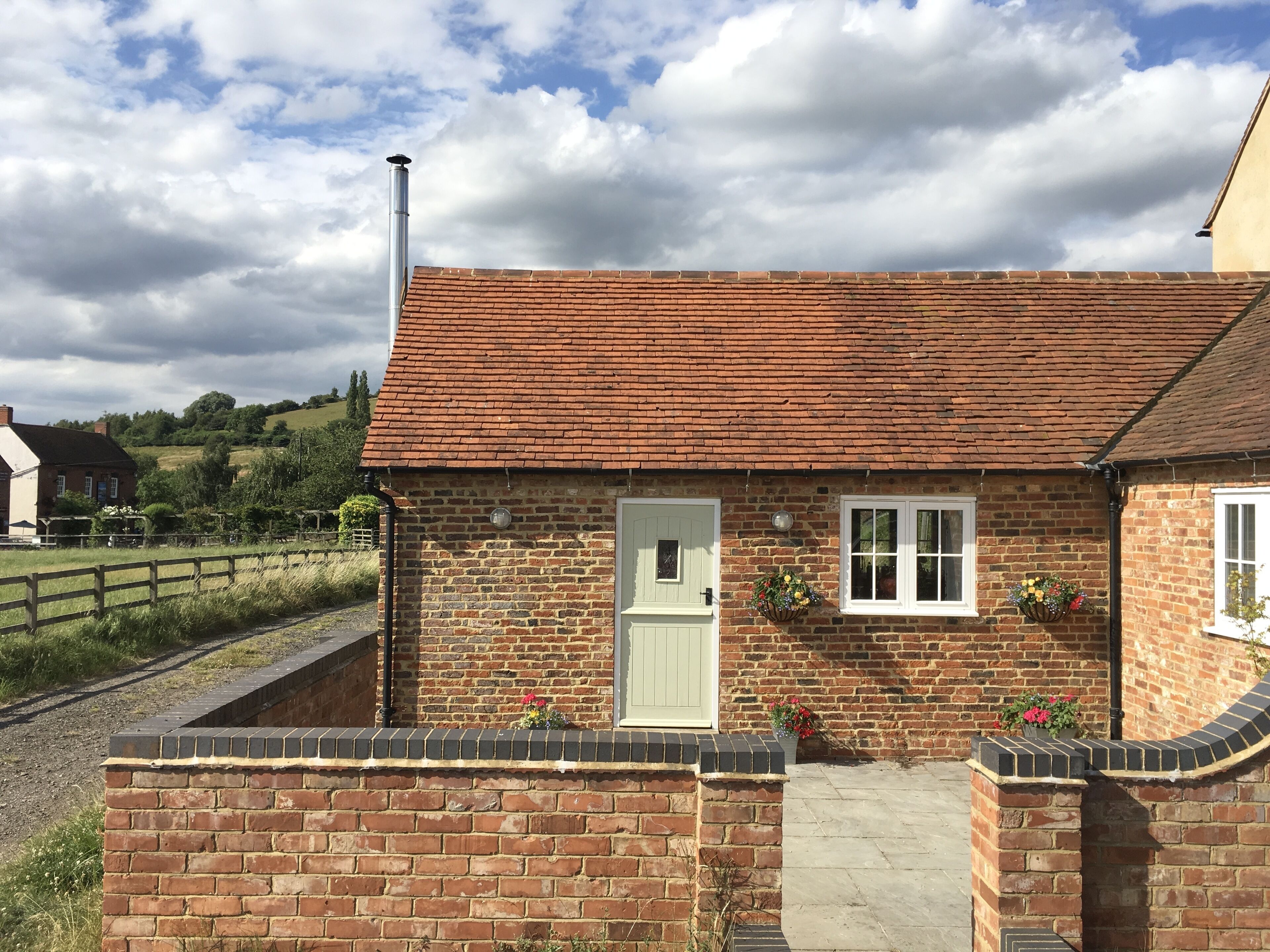 A brick house with a red-tiled roof, a white door, and two windows with flower boxes.