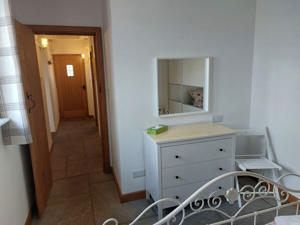 A bedroom with a bed, a bedside table, a dresser, and a mirror.
