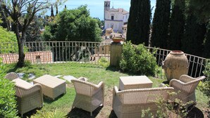 A terrace with wicker furniture, a large vase, and a view of a town and lake.