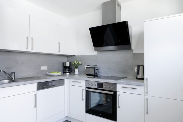 A modern kitchen with white cabinets, a built-in oven, a coffee maker, and a toaster. - HarzHaus 1 - Pure relaxation between the city and nature (Wernigerode)