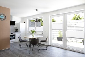 A modern kitchen with white cabinets, a stove, and a dining area with a round table and four chairs. - HarzHaus 1 - Pure relaxation between the city and nature (Wernigerode)