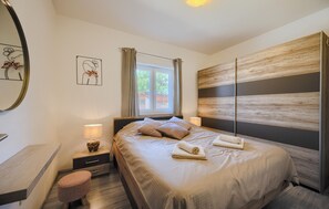 A bedroom with a bed, a nightstand, a lamp, a wall clock, and a window with curtains.